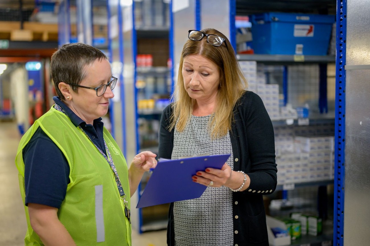 Two warehouse employees reviewing information on a clipboard