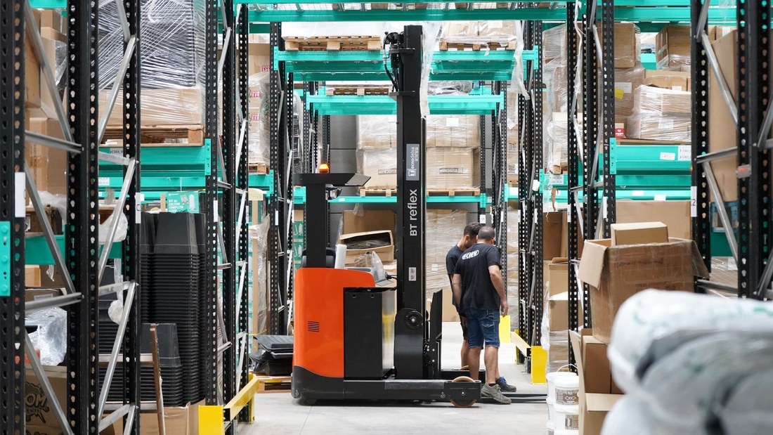 Warehouse worker and a reach forklift between stocked pallet racks